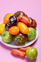 Multicolored assortment of French fresh ripe tomatoes, healthy vegetables for salad on pink background