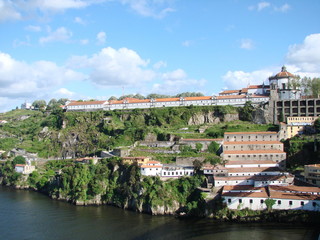 Fototapeta na wymiar Panorama of a tall rocky shore of the river covered with city houses surrounded by green plantations against the background of a blue sky.
