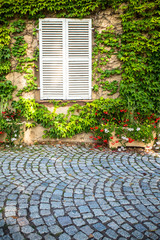 Fototapeta na wymiar Cobblestones and White shutters in window on exterior building wall covered in ivy