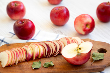Slices of red apples on rustic wooden board over white wooden background, side view. Close-up.