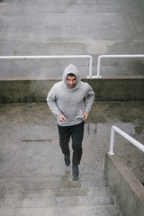Urban athlete running upstairs under the rain. Banner of sporty man working out outside and climbing stairs in cold winter.