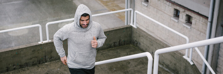 Urban athlete running upstairs under the rain. Banner of sporty man working out outside and climbing stairs in cold winter.