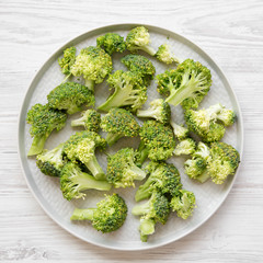 Freshly cut raw broccoli on gray plate on a white wooden table, top view. Flat lay, from above. Close-up.