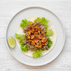 Shrimp taco with lime on round gray plate on a white wooden table, overhead view. Flat lay, top view, from above. Mexican cuisine.