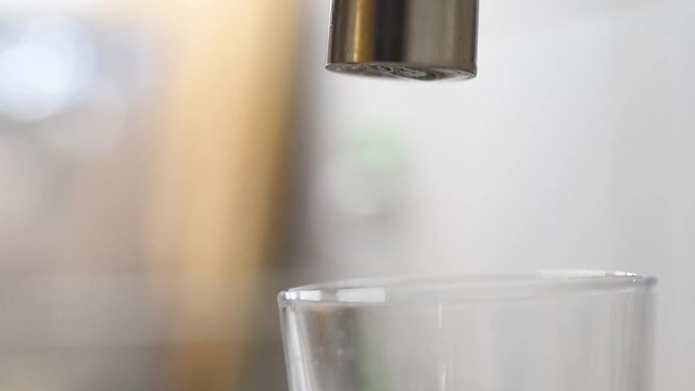 Wasser tropft aus einem Hahn in ein Glas