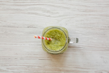 Glass jar of green celery smoothie on white wooden background, overhead view. Flat lay, from above, top view.