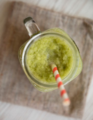 Glass jar of green celery smoothie on white wooden table, top view. Flat lay, overhead.