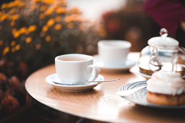 Cup of tea with cake on wooden table in cafe with flowers at background. Good morning.