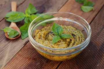 Basil pesto in glass bowl on a wooden table. Close up food.
