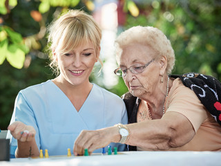 Pflegerin spielt mit Seniorin ein Brettspiel