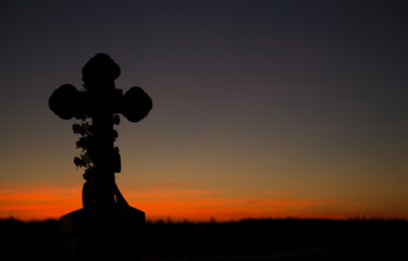 A stone Orthodox cross standing at crossroads on the background of the sky blackened by the setting...