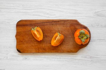 Fresh persimmon on a chopping board over white wooden surface, top view. Flat lay, overhead, from above.