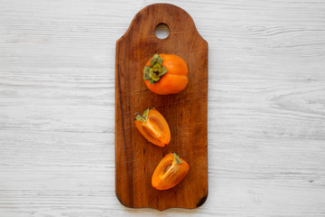 Fresh persimmon on a chopping board on white wooden table, top view. Flat lay, overhead, from above. Copy space.