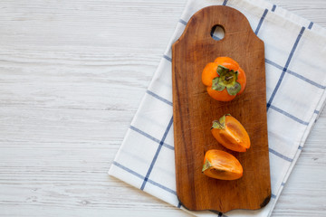 Fresh persimmon on a chopping board on white wooden background, overhead view. Copy space.