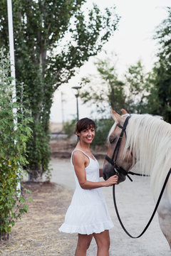 Portrait of happy woman in white dress leading horse