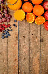 Orange juice, fresh oranges, apples, grapes, raspberries and blueberries on a wooden table - fruit background - view from above - vertical photo