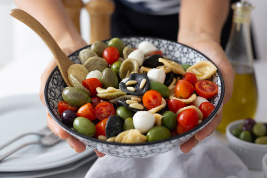 Woman showing Mediterranean orecchiette with tomato, olives and mozzarella - Powered by Adobe