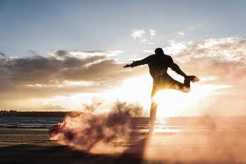 Man doing movement training at the beach with colorful smoke at sunset