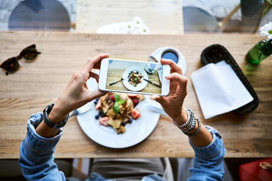 Overhead view of woman taking picture of food with smartphone in cafe
