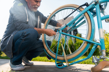 Repairing bicycle. Bearded mature man wearing jeans and dark blue sport jacket repairing his blue bicycle