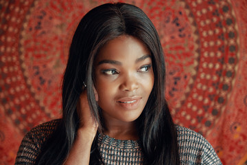 Portrait of young elegant black woman with long hair looking away against colorful wall