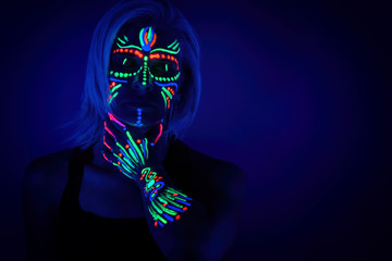 Portrait of woman with ethnic pattern, neon makeup in ultraviolet light. Body Art design of female posing in UV, painted face and hand, colourful make up - obrazy, fototapety, plakaty