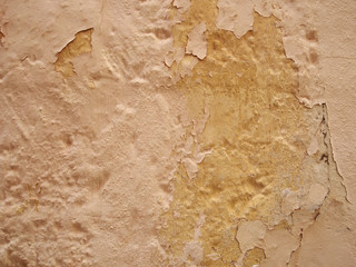 cracked peeling paint texture in shades of beige and yellow on an old textured concrete wall