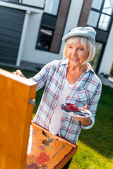 Color palette. Beaming retired blonde-haired lady holding color palette while having inspiration...