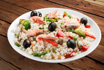 Rice porridge with shrimps and vegetables. On a wooden background