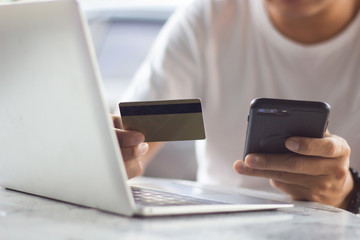 Man using mobile phone and laptop shopping online with credit card. Man holding credit card using smart phone for purchase or buy and sell products & services.
