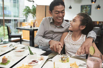 Happy father eating together with his cute smiling daughter at the table at restaurant