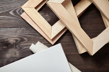 Wooden stretchers and a white blank artistic canvas lying on a dark wooden table. Wood products: Subframes. Top view