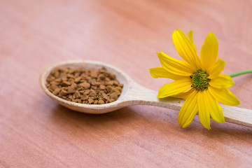 Wooden spoon with coffee and yellow flower on the table
