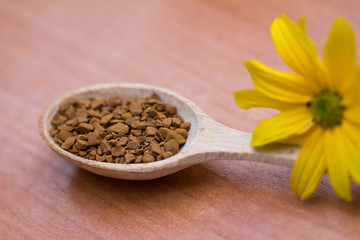Wooden spoon with coffee and yellow flower on the table