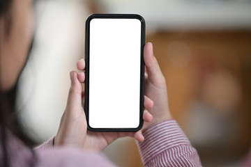 Cropped shot of female hand holding blank white screen mobile phone over blurred bokeh background