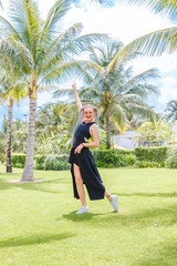 girl with pigtails in a black dress and sunglasses is having fun between the palm trees