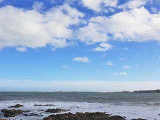 Fluffy white clouds in blue sky over sea with lighthouse in background