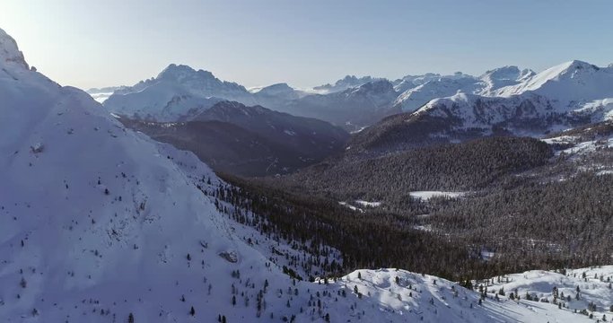 Backward aerial to snowy alpine valley with woods forest at Valparola pass.Sunny sunset or sunrise,clear sky.Winter Dolomites Italian Alps mountains outdoor nature establisher.4k drone flight
