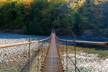Narrow metal foot bridge across river in autumn