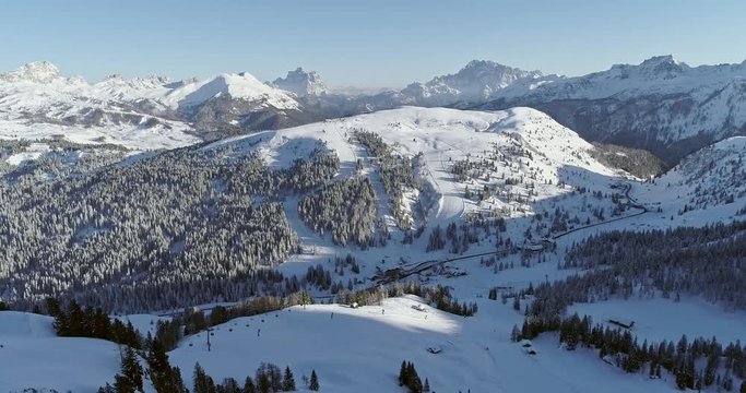 Backward aerial to snowy alpine valley with ski tracks, chair lifts at Piz Boe.Sunny day,clear sky.Winter Dolomites Italian Alps mountains outdoor nature establisher.4k drone flight