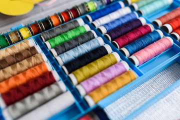 View on rainbow of thread spools arranged in a needlework box, ready for sewing.