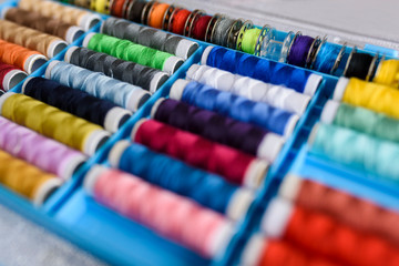 A lot of colorful thread spools for needlework arranged in a box, a bit blurred with few spools in focus. - obrazy, fototapety, plakaty