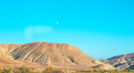View of relief mountains in a steppe arid region. Moon in the sky