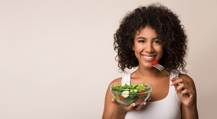African-american woman eating vegetable salad over light background - obrazy, fototapety, plakaty