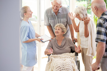 Smiling nurse talking with happy senior woman in the wheelchair and elderly people