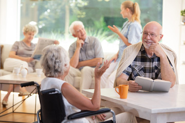 Smiling senior man with book talking with elderly woman in the wheelchair