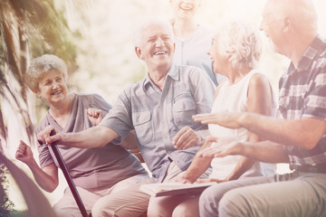 Smiling senior man with walking stick relaxing with elderly woman and friends