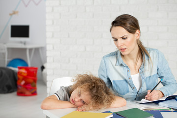 Nervous mother doing homework with bored kid with Asperger syndrome