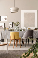 Grey and yellow chair at table under lamp in dining room interior with posters and plants. Real photo - obrazy, fototapety, plakaty