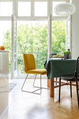 Vertical view of dining room table with yellow and black chairs and green tablecloth, stylish...